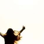 Backlit silhouette of a woman with arms up, capturing freedom and joy in a minimalist setting.